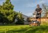 A man mowing a lawn with a lawn mower, showing the difference between overgrown grass and freshly cut grass