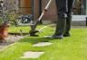 Gardener trimming lawn edge with electric trimmer