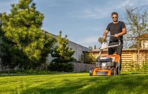 A man mowing a lawn with a lawn mower, showing the difference between overgrown grass and freshly cut grass