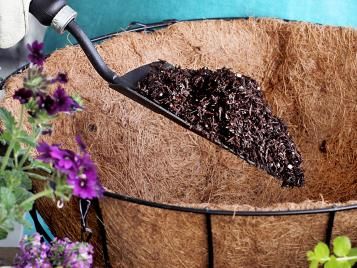 Close-up of gardener’s hand using trowel to fill hanging basket with compost.