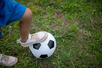 Close-up of child’s foot resting on football on lawn